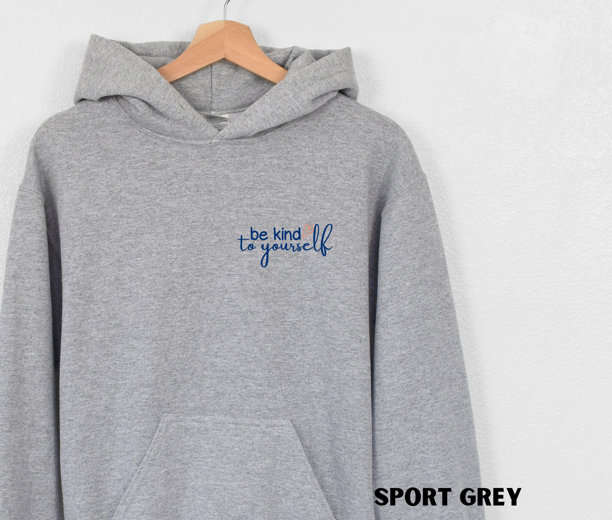 Embroidered Hoodie in sport grey with "be kind to yourself' in navy blue text with a pink heart on the upper left chest. 