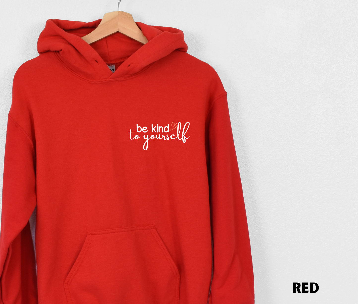 Embroidered Hoodie in red with "be kind to yourself' in white text with a pink heart on the upper left chest. 