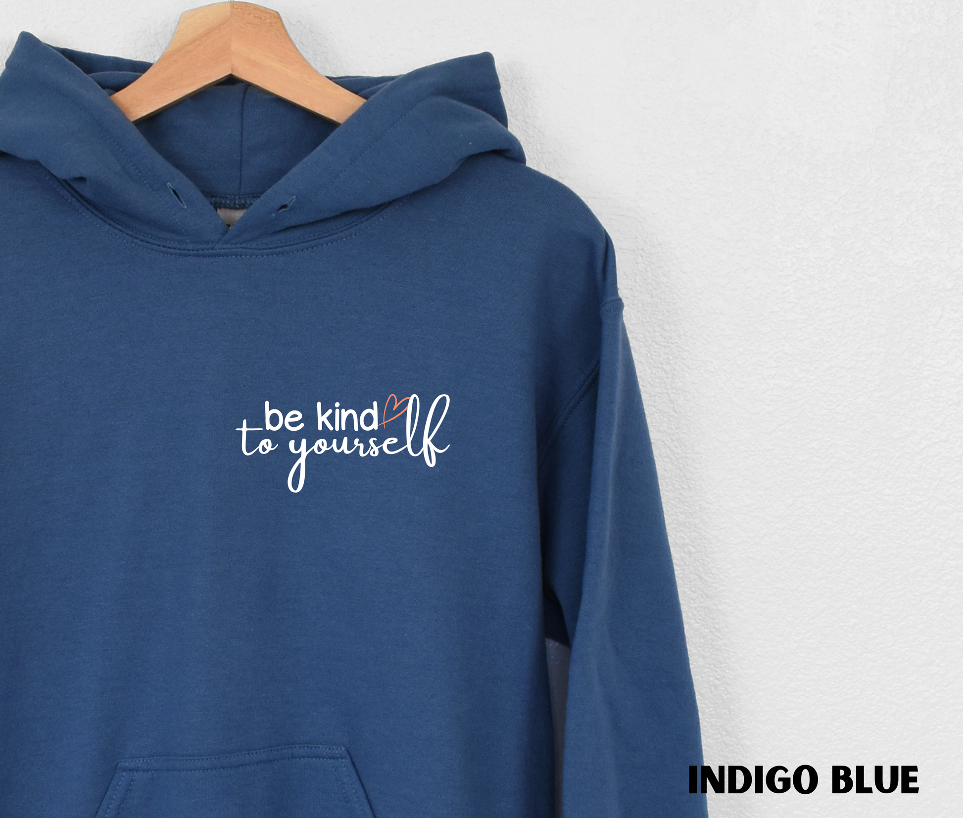 Close up of an Embroidered Hoodie in indigo blue with "be kind to yourself' in white text with a pink heart on the upper left chest. 