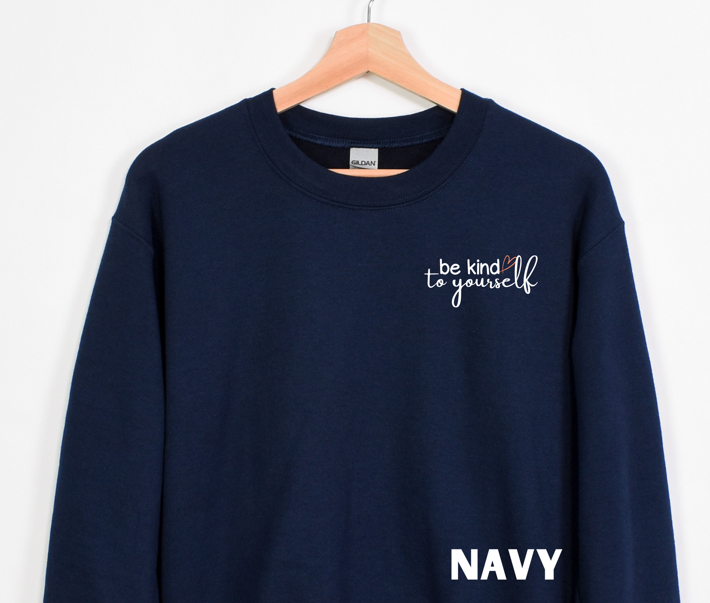 A navy blue embroidered crewneck sweatshirt with the words "be kind to yourself" embroidered in white with a pink heart on the left chest.