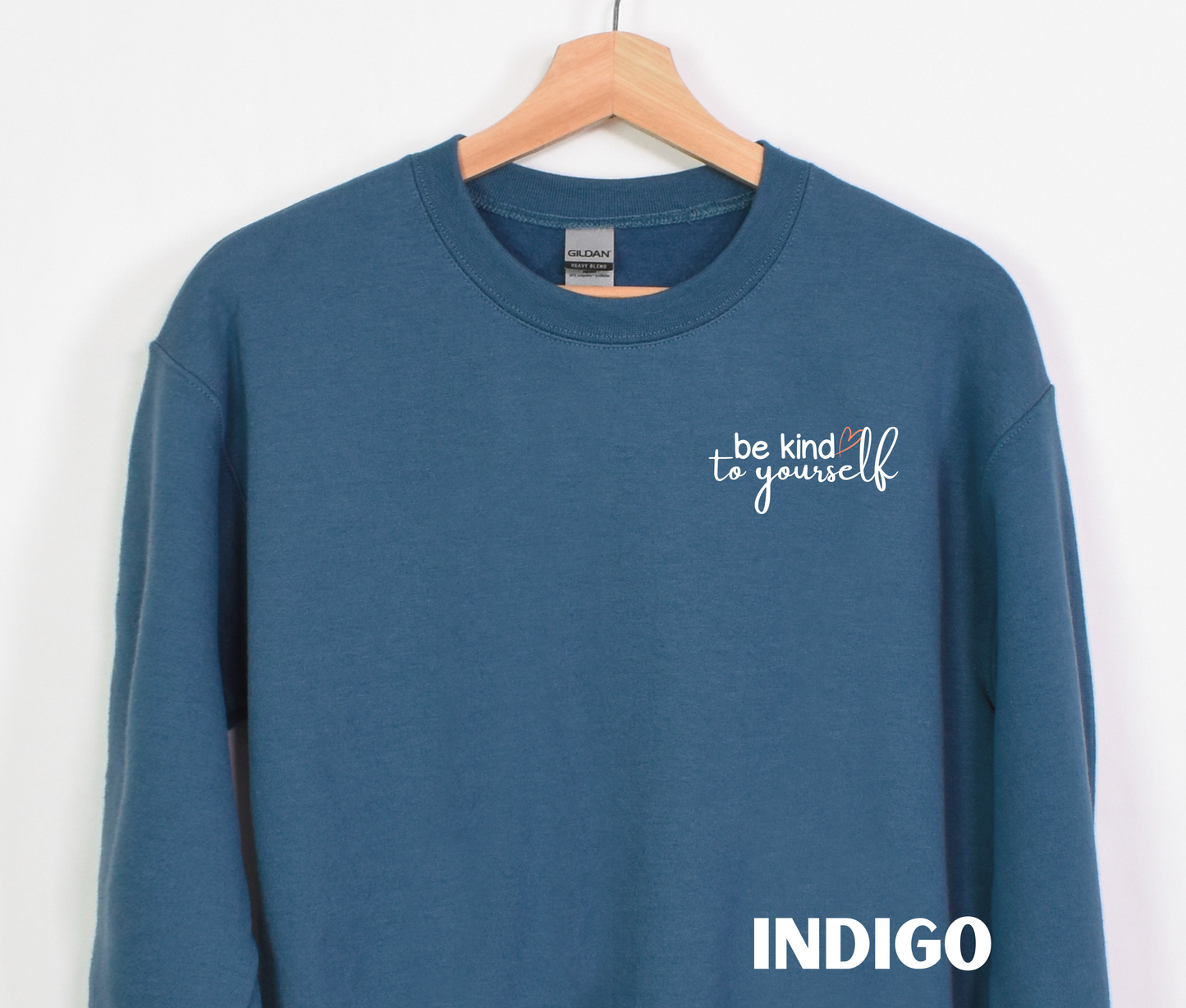 An indigo blue embroidered crewneck sweatshirt with the words "be kind to yourself" embroidered in white with a pink heart on the left chest.