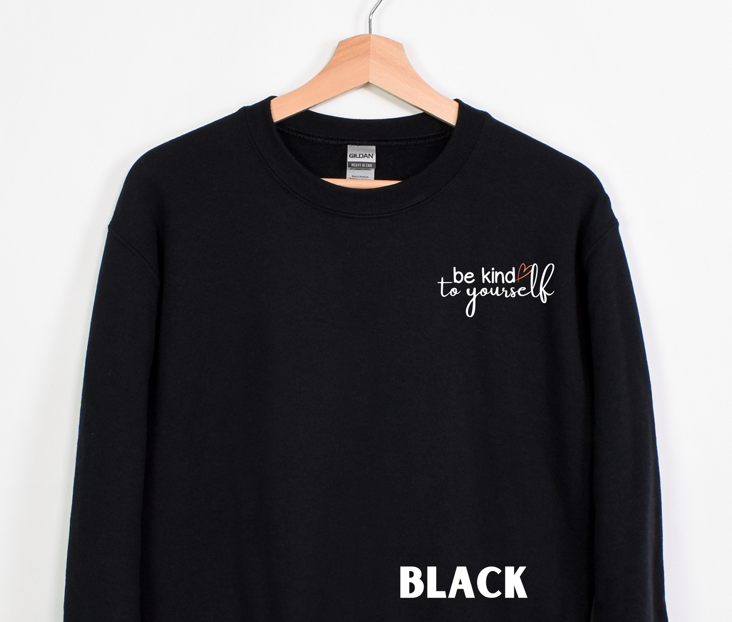 A black embroidered crewneck sweatshirt with the words "be kind to yourself" embroidered in white with a pink heart on the left chest.